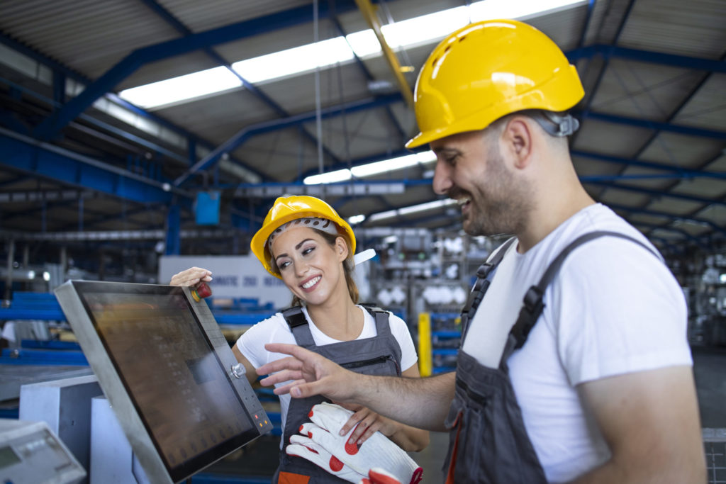 Factory worker explaining trainee how to operate industrial mach